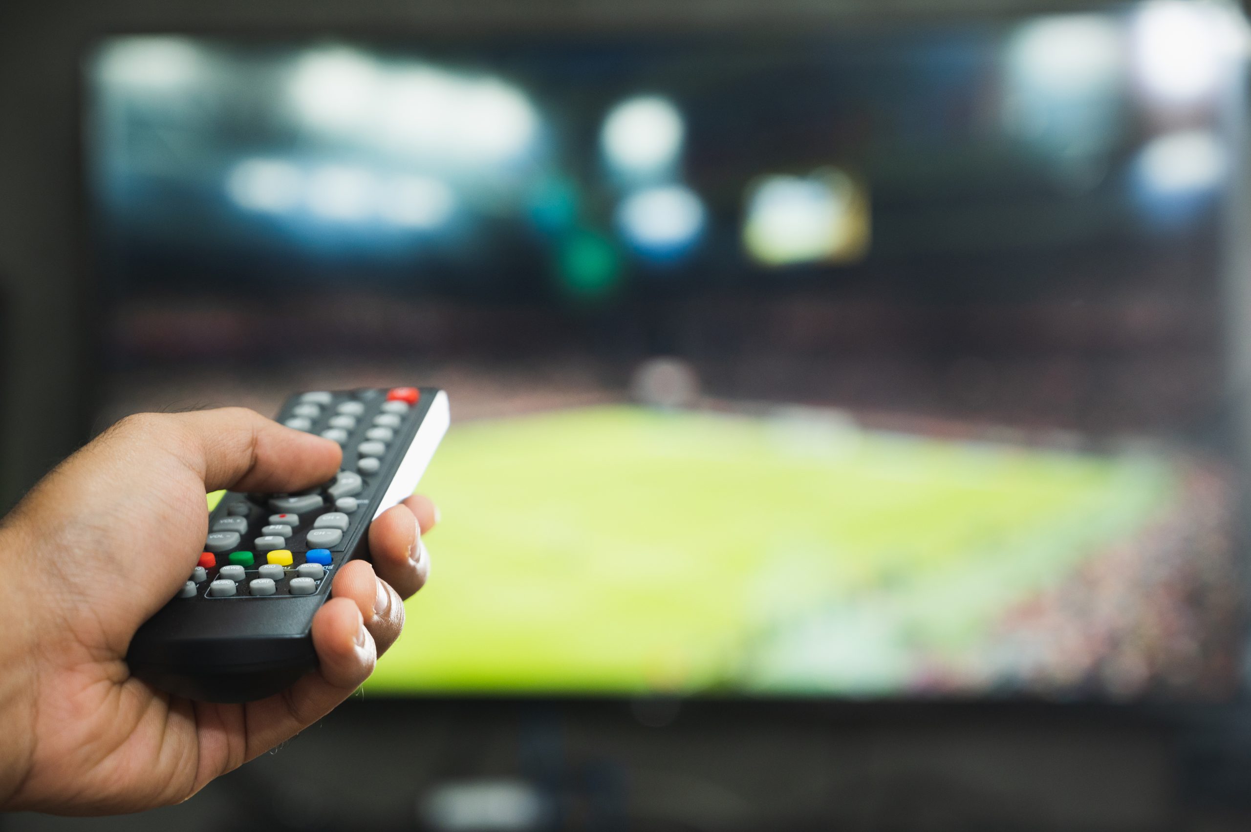 Young man holding television remote control watching football program. Hands pointing to tv screen set and turning it on or off select channel watching tv in the living room relax.